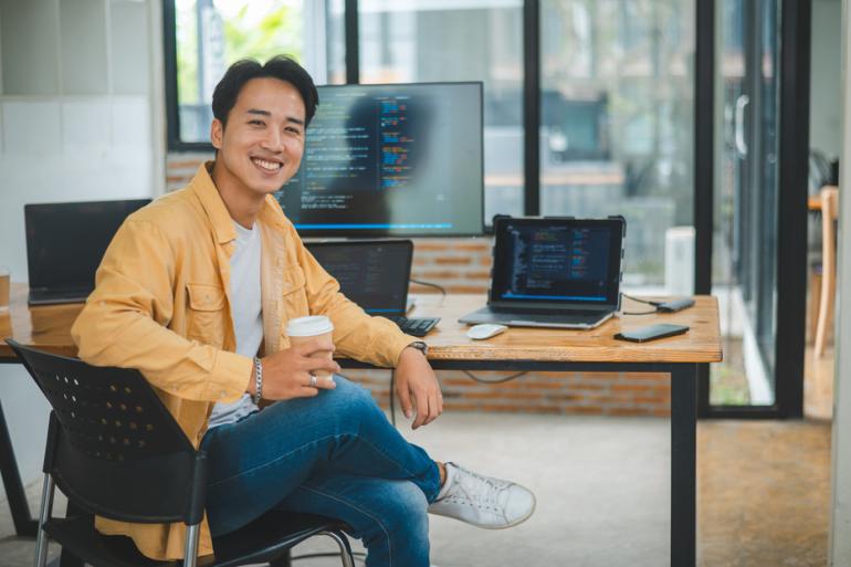 Hombre sonriendo sentado con pantallas detrás de el